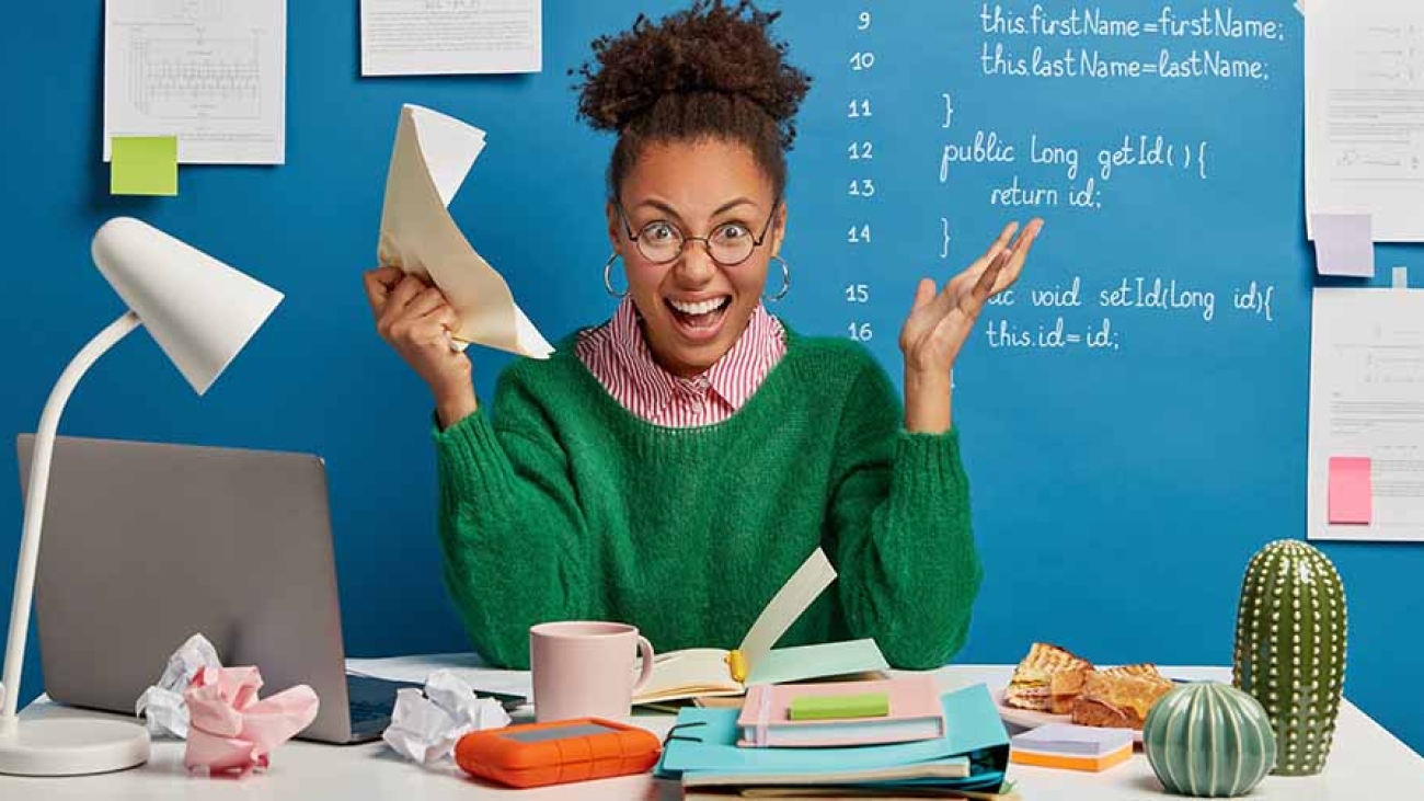 Mad female entrepreneur gets crazy because of much work, screams angrily, holds crumpled paper, stressed of havig deadline, has problem with computer, poses at workplace, stuck with hard task
