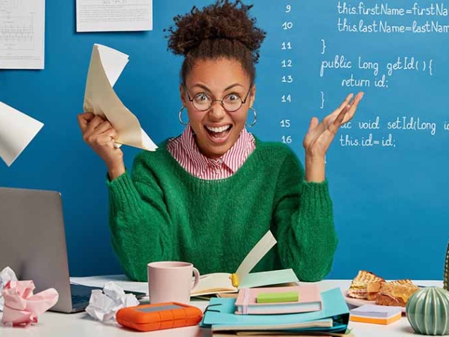 Mad female entrepreneur gets crazy because of much work, screams angrily, holds crumpled paper, stressed of havig deadline, has problem with computer, poses at workplace, stuck with hard task