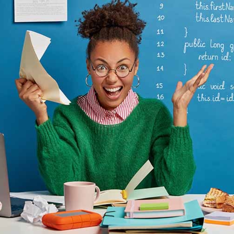 Mad female entrepreneur gets crazy because of much work, screams angrily, holds crumpled paper, stressed of havig deadline, has problem with computer, poses at workplace, stuck with hard task